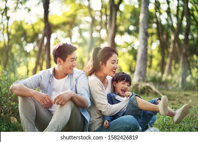 Young Asian Parents And Son Having Fun Outdoors In Park