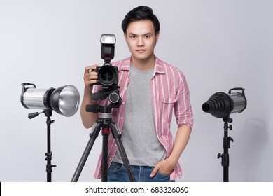 Young Asian Photographer Holding Digital Camera, While Working In Studio