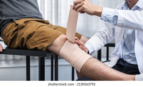Young asian physiotherapist bandaging knee of man patient with in injury while healing treatment and to giving rehabilitation therapies in clinic - Shutterstock ID 2130563792