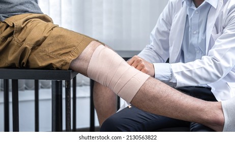 Young asian physiotherapist bandaging knee of man patient with in injury while healing treatment and to giving rehabilitation therapies in clinic - Shutterstock ID 2130563822