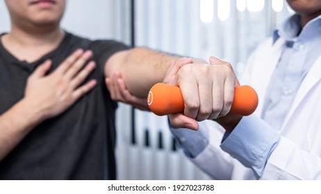 Young asian physiotherapist helping male patient stretching arm during exercise correct with dumbbell in hand during training hand to rehabilitation therapies in clinic - Powered by Shutterstock