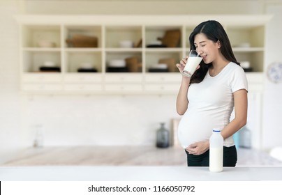 Young Asian Pregnant Woman Drinking Milk At Kitchen.