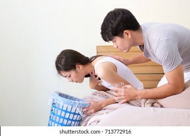 Young asian pregnant woman feel sick on bed in the room and husband holding a glass of water for take care of pregnant wife.