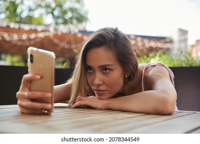 young asian pretty woman with long hair lays her head on her arms and table, holding phone in hand. beautiful pensive melancholic lady laying at cafe, using smartphone. lifestyle portrait