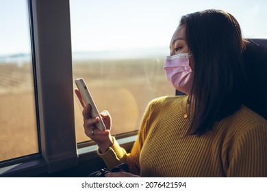 Young Asian pretty woman travelling in empty bus with pink mask using smartphone