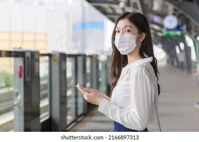 Young Asian professional business woman stands on a sky train station in town wearing a face mask while uses her smartphone to send messages  to the customer office - Powered by Shutterstock