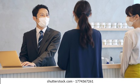 Young Asian Receptionist Talking With Customers With Surgical Mask. Hotel Worker. Store Clerk.