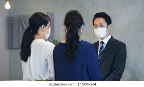 Young Asian Receptionist Talking With Customers With Surgical Mask. Hotel Worker. Store Clerk.