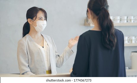 Young Asian Receptionist Talking With Customers With Surgical Mask. Hotel Worker. Store Clerk.