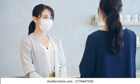 Young Asian Receptionist Talking With Customers With Surgical Mask. Hotel Worker. Store Clerk.