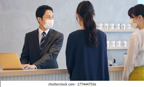 Young Asian Receptionist Talking With Customers With Surgical Mask. Hotel Worker. Store Clerk.