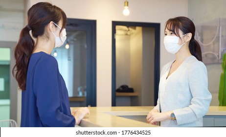 Young Asian Receptionist Talking With Customers With Surgical Mask. Hotel Worker. Store Clerk.