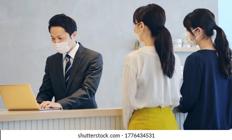 Young Asian Receptionist Talking With Customers With Surgical Mask. Hotel Worker. Store Clerk.