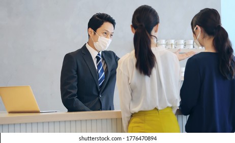 Young Asian Receptionist Talking With Customers With Surgical Mask. Hotel Worker. Store Clerk.