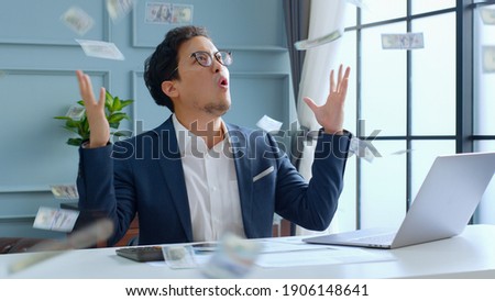 Young Asian rich businessman enjoy with money rain while working in office, millionaire concept