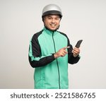 Young asian rider wearing green jacket uniform and helmet standing holding smartphone food application on isolated. Male delivery service worker. Delivery courier and shipping food service.