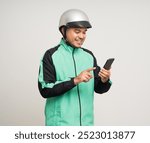 Young asian rider wearing green jacket uniform and helmet standing holding smartphone food application on isolated. Male delivery service worker. Delivery courier and shipping food service.