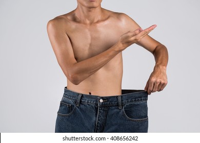 Young Asian Shirtless Man With Over-sized His Old Jeans After Lose Weight And Hand Up With Copy Space To Welcome To Weight Loss Exercise Concept