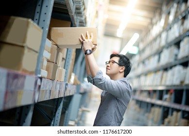 Young Asian shopper man picking cardboard box package from product shelf in warehouse. Male customer shopping lifestyle in department store. Buying or purchasing factory goods. Shopaholic concepts