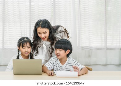 Young Asian Single Mother Teaching Or Helping Daughter And Son Doing Home Work With Technology Laptop In Home, Home School Education, Relationship And Family, Communication And Conversation Concept