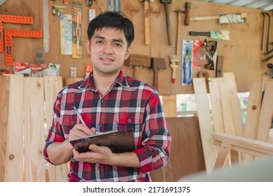 Young Asian Small Business Owner In The Woodwork Workshop And Calling On Phone With Customer.