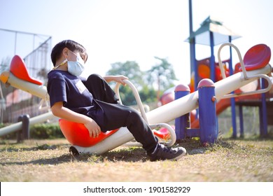 Young Asian Small Kid Wearing Facial Mask To Protect From Covid19 Coronavirus As New Normal Lifestyle Sitting In Kid Playground Alone During Beautiful Sunny Day