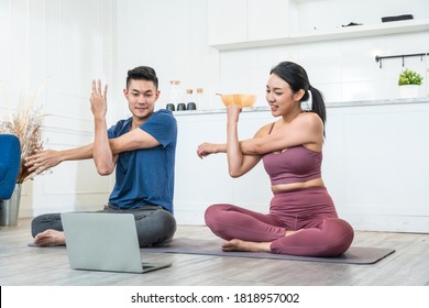 Young Asian sporty couple watching live or video tutorial practice yoga lesson at home together. healthy man and woman Stretching and balancing body on exercise mat. wellness relaxing lifestyle