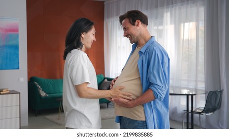Young asian strokes the belly of pregnant transgender husband standing together in modern apartment. Lgbt. An unconventional family.  - Shutterstock ID 2199835885