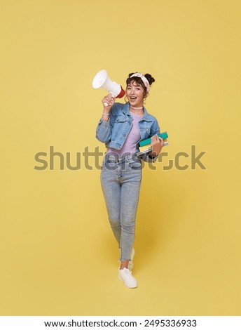 Young Asian student woman shouting into megaphone making announcement in isolated on yellow background.