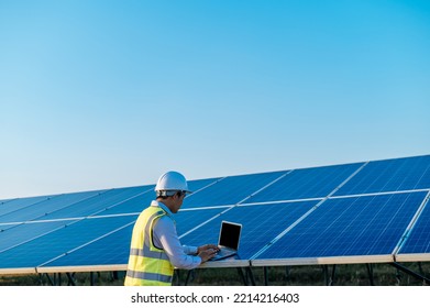 Young Asian Technician Man Checking Operation Of Sun And Cleanliness Of Photovoltaic Solar Panel And Typing On Laptop Computer While Working In Solar Farm