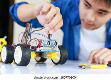 Young asian teen plugging energy and signal cable to sensor chip of toy car workshop.