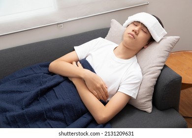 Young asian teenage boy feeling sick in blanket with white towel on the forehead. - Shutterstock ID 2131209631