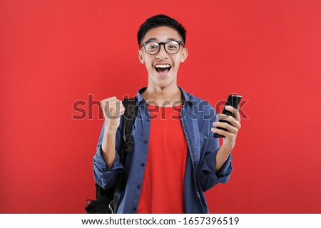 Young Asian teenager doing winning gesture holding mobile phone, Happy get special gift online, isolated on red background
