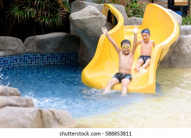 Young Asian Thai Boy Play Water Slider In A Park During Summer Time.