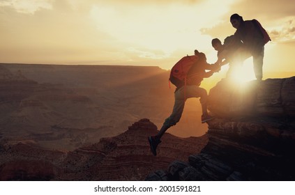 Young asian three hikers climbing up on the peak of mountain. People helping each other hike up a mountain at sunrise. Giving a helping hand. Climbing ,Helps and team work concept
