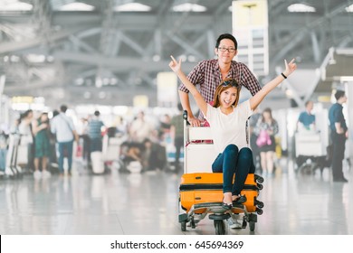 Young Asian Tourist Couple Happy And Excited Together For The Trip, Girlfriend Sitting And Cheering On Baggage Trolley Or Luggage Cart. Holiday Vacation Traveling Abroad Concept, With Copy Space