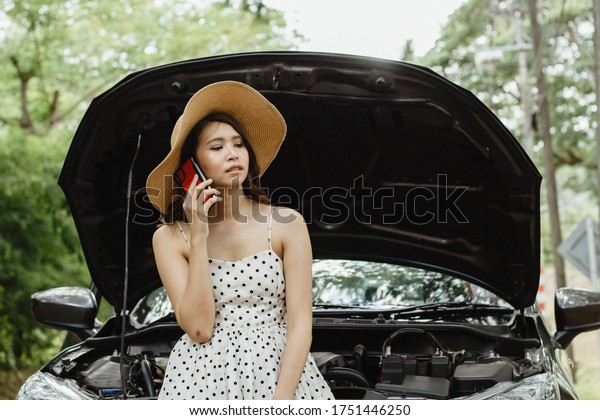 A young Asian tourist is talking on the\
phone to call her car insurance company to check the condition of\
her car. Caused by unknown\
reasons