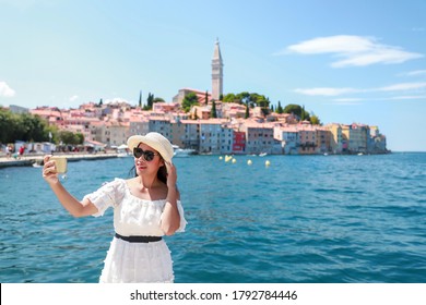 Young Asian tourist woman taking picture or selfie at Harbour rovinj city, Croatia by smartphone. Happy freedom girl traveling in Europe in summer time with copy space for text.