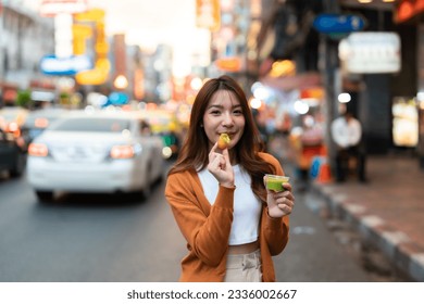 Young Asian tourists standing and eating Thai desserts. Young beautiful tourists in Chinatown street food market, Bangkok, Thailand