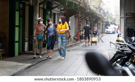 Young Asian tourists wearing protection face mask walking among local street alley in Bangkok.