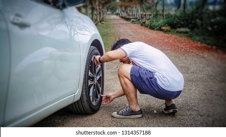 Young Asian Traveler Man Checking Air Pressure Of Car Tire On Local Road Side While Travel Countryside