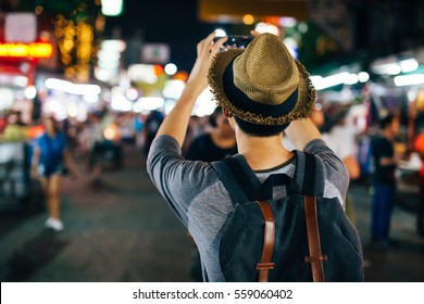 Young Asian traveler taking photo with mobile phone in Khaosan road at night in Bangkok, Thailand