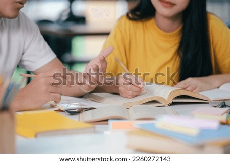 Young asian university students are studying for an exam. There are tutor books with friends. They are classmates that try to help each other. They have been tutoring for many hours in the campus.