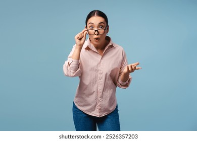 Young Asian woman is adjusting her glasses with a shocked expression on her face, gesturing with her hand as if she has just heard surprising news - Powered by Shutterstock