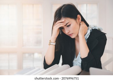 Young asian woman architect holding forehead and neck while working on project at office desk. She is tired and tired.