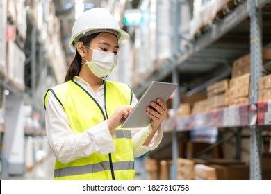 Young asian woman auditor or trainee staff wears mask working during the COVID pandemic in store warehouse shipping industrial. looking up and checks the number of items store by digital tablet.