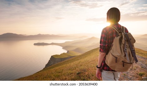 A young Asian woman with a backpack hiking in the summer and enjoying the view of the sunset sea and mountains. Mountain and coastal travel, freedom and an active lifestyle - Powered by Shutterstock