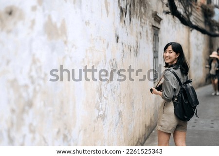Young Asian woman backpack traveler using digital compact camera, enjoying street cultural local place and smile. Journey trip lifestyle, world travel explorer or Asia summer tourism concept. 