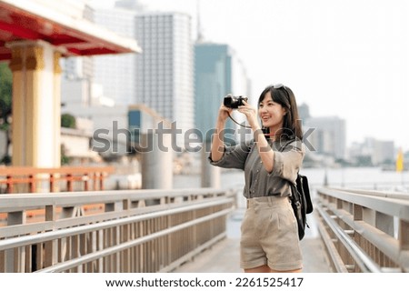 Young Asian woman backpack traveler using a camera in express boat pier on Chao Phraya River in Bangkok. Journey trip lifestyle, world travel explorer or Asia summer tourism concept. 