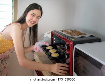 Young Asian Woman Baking Cookies In Oven At Home